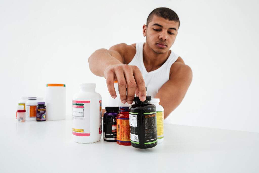 Sportler stehend weiße Wand hält Vitamine 1 skaliert